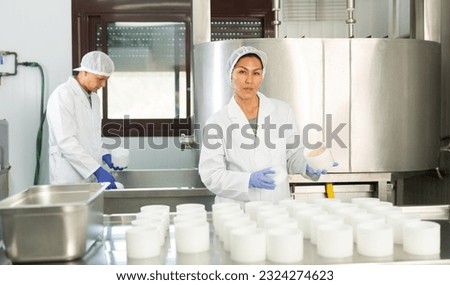 Portrait of skilled Asian woman wearing white uniform working in shaping workshop of cheese dairy..