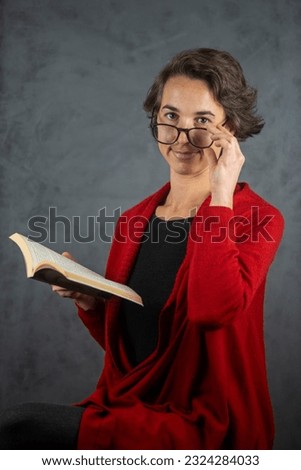young woman in glasses and red jacket, reading a book on a gray background