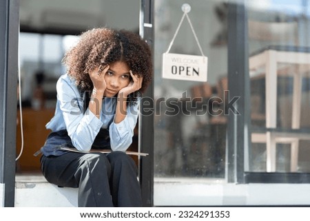 African barista woman in a barista uniform holding file showing stress and frustration sitting the entrance of a coffee shop there are no customers at the store Royalty-Free Stock Photo #2324291353