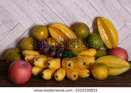 tropical fruit on wooden table. bananas, oranges, red apples, pears, grapes, and star fruit.