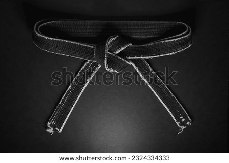 Beautifully knotted old shabby black belt of a martial artist on a dark background. Royalty-Free Stock Photo #2324334333