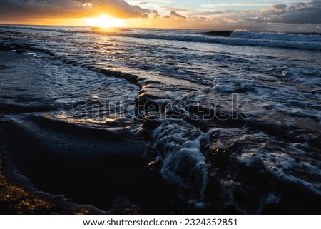 Golden hour on beach. Close up shot of reflection in water. Dramatic sea sunrise. Burning sky and shining golden waves. Reflection of sunlight over water surface.