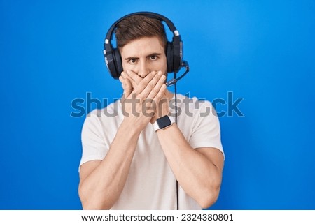 Hispanic man with beard listening to music wearing headphones shocked covering mouth with hands for mistake. secret concept. 