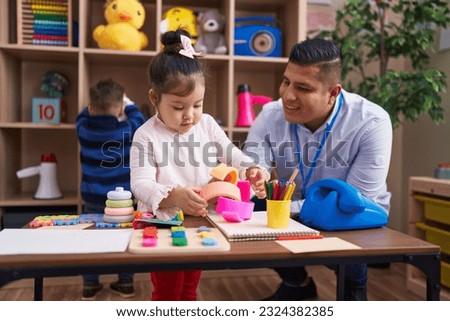 Hispanic man with boy and girl playing with construction blocks sitting on table at kindergarten Royalty-Free Stock Photo #2324382385