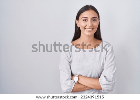 Young hispanic woman standing over white background happy face smiling with crossed arms looking at the camera. positive person. 