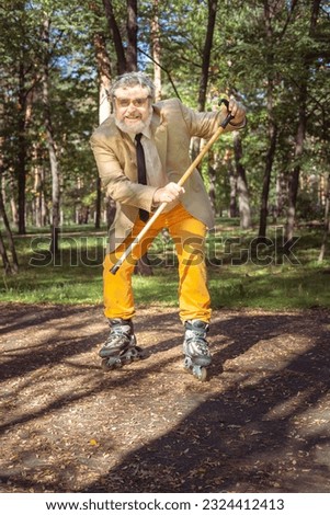 Funny old man is roller skating in the park. An active grandfather with a walking stick dances and makes faces. Grandfather with a white beard.
