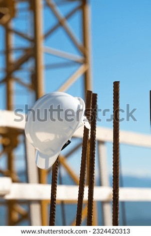 Close-up of a white helmet hanging on a rebar on a construction site against the background of a construction crane and a blue sky. Construction concept, safety techniques