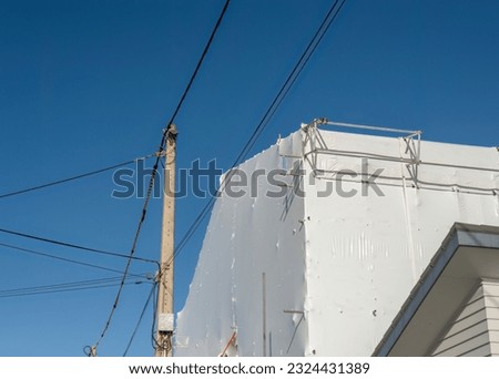 Residential house under repair with metal scaffolding and white sheet cover around it.