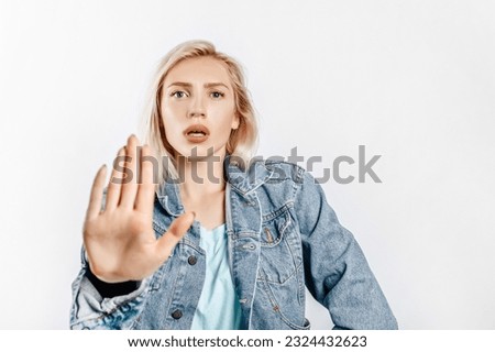 Beautiful young girl unhappy frown and says stop with a hand gesture on gray isolated background