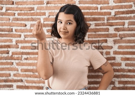 Young hispanic woman standing over bricks wall doing italian gesture with hand and fingers confident expression 