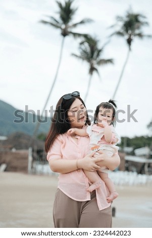 Happy young mother play with her little baby daughter on the beach, hugs and kiss