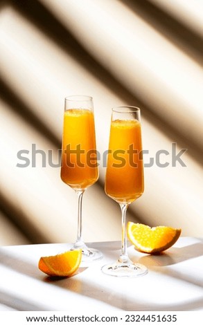 Mimosa summer cocktail drink with orange juice and cold dry champagne or sparkling wine in glasses. Beige background, hard light, shadow pattern Royalty-Free Stock Photo #2324451635