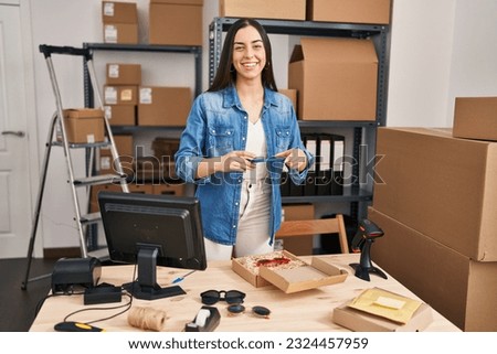 Young beautiful hispanic woman ecommerce business worker make photo to package at office