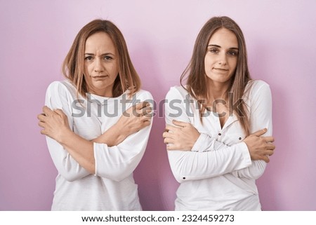 Middle age mother and young daughter standing over pink background shaking and freezing for winter cold with sad and shock expression on face 