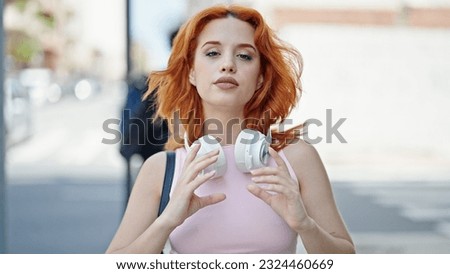 Young redhead woman wearing headphones at street