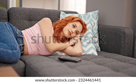 Young redhead woman watching tv lying on sofa at home