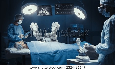 Surgeon Wearing AR Headset And Using High-Precision Remote Controlled Robot Arms To Operate On Patient, While His Colleague Checking Vitals On Tablet In Hospital. Doctors Working With Robotic Limbs. Royalty-Free Stock Photo #2324465549