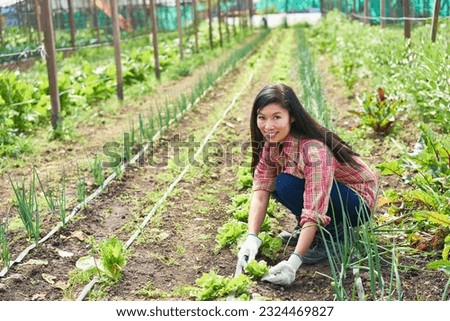 Portrait of smiling female farmer crouching amidst plants at greenhouse