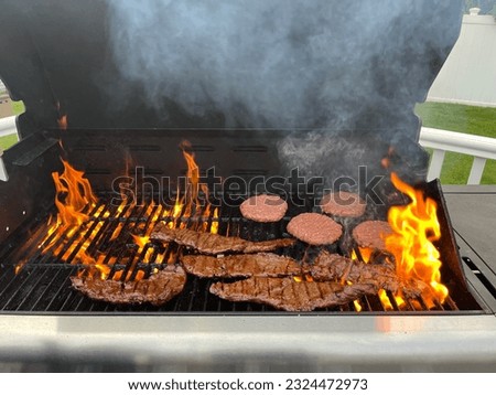 The top down of a grill with steaks and hamburgers cooking on it.