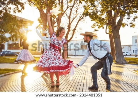 group of Latin American young adults wearing huaso costume dancing cueca in the town square at sunset Royalty-Free Stock Photo #2324481851