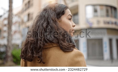 Young beautiful hispanic woman standing backwards with serious expression at street