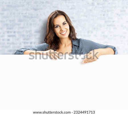 Beautiful woman stand beehind, peep out, hang over blank empty banner with copy space, white bricks wall background. Executive person, businesswoman, bank manager show ad board advertise concept.
