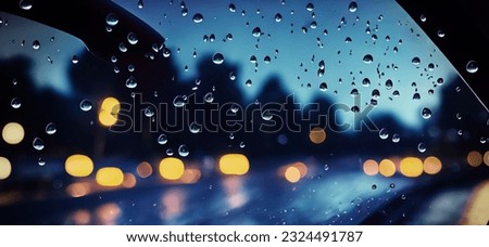 Rain shower on car windshield or car window and blurry road in background. Driving in rainy season. Rain drops on car mirror. Traffic road in evening rain. Drizzle raining decreases driving visibility