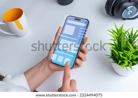 Woman holding a smartphone with a conceptual user interface. The interface showcases a clean design with vibrant colors and intuitive navigation elements Royalty-Free Stock Photo #2324494075