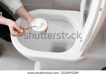 Woman cleaning white toilet bowl with baking soda Royalty-Free Stock Photo #2324495289