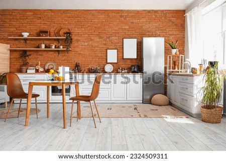Interior of kitchen with stylish fridge, counters, shelves, table and blank pictures