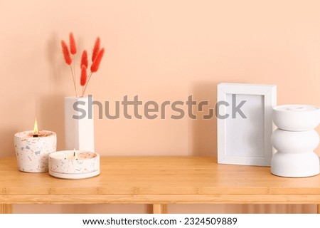 Holders with burning candles and blank frame on table near beige wall in room Royalty-Free Stock Photo #2324509889