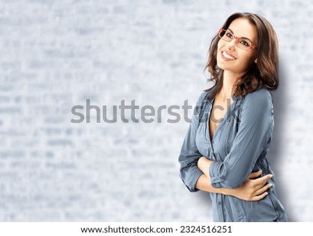 Portrait of happy smiling brunette woman looking up, in red eye glasses, confident wear, white bricks wall background. Studio portrait image. Copy space blank area. Ophthalmology ad.