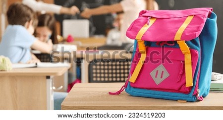 Child's backpack on desk in classroom Royalty-Free Stock Photo #2324519203