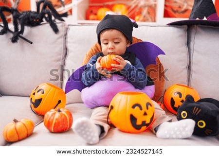 Adorable hispanic boy wearing costume holding pumpkin at home