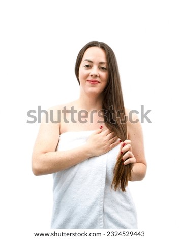 Cute young brunette woman smiling while wearing a bathroom towel against a white background