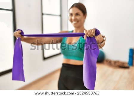 Young beautiful hispanic woman smiling confident using elastic band training at sport center