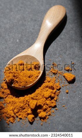 Turmeric powder in wooden spoon on black background and sunlight in kitchen. selective focus. soft picture.
