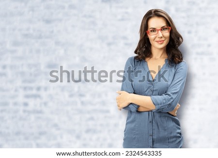 Portrait of happy smiling young brunette woman in red eye glasses, confident wear, white bricks wall background. Business studio concept. Copy space blank area for text. Ophthalmology ad.