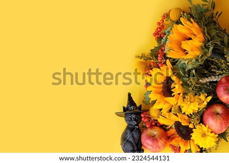 Magic black cat figurine, apples and autumn flowers bouquet on abstract yellow background. fall season. symbol of autumn season, thanksgiving, halloween, mabon. top view. copy space