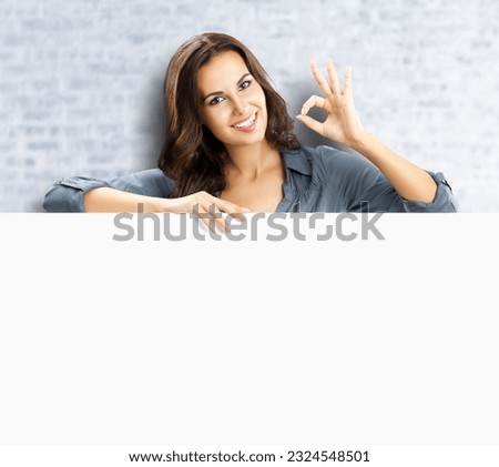 Beautiful woman stand beehind, peep out, hang over blank empty banner with copy space, white bricks wall background. Executive person, businesswoman, bank manager show ok okay hand sign gesture.