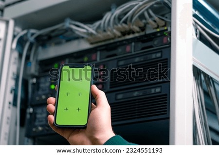 Data center close-up hacker or engineer holding phone with green screen hand stealing information from servers cloud storage technology