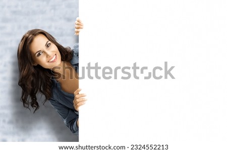 Beautiful woman stand beehind, peep out blank empty banner with copy space, white bricks wall background. Executive person, confident businesswoman, bank manager showing ad board, advertise concept.