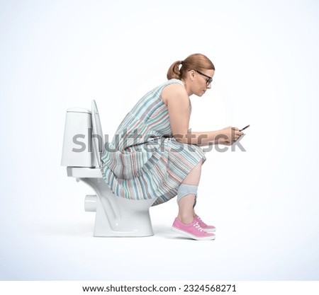 A young woman in glasses and colorful dress on the toilet and looks at her smartphone, side view, isolated on a light blue background