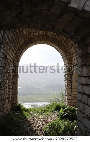 View from old medieval arch to mountain valley with sun light through the hole and shadow from wall on grassy ground