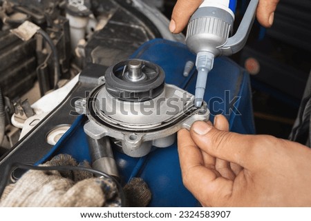 An auto mechanic applies silicone black sealant to a new engine cooling pump before installing it Royalty-Free Stock Photo #2324583907