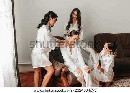 The bridesmaids look at the smiling bride. The bride and her fun friends are celebrating a bachelorette party in matching dresses. Bride and friends in the room Royalty-Free Stock Photo #2324584693