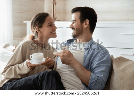 Quiet happiness. Happy tender married couple millennial man and woman enjoy being at home together cuddling smiling sitting on sofa at new dwelling having pleasant conversation drinking morning tea Royalty-Free Stock Photo #2324585261