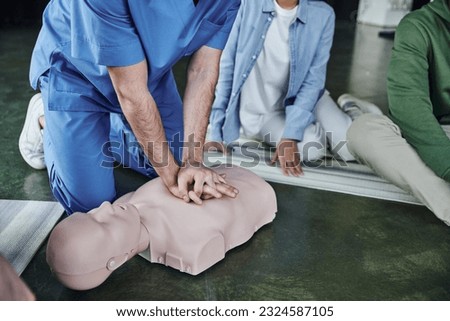 cardiopulmonary resuscitation, partial view of medical instructor doing chest compressions on CPR manikin near young participants of first aid seminar, life-saving skills and techniques concept Royalty-Free Stock Photo #2324587105