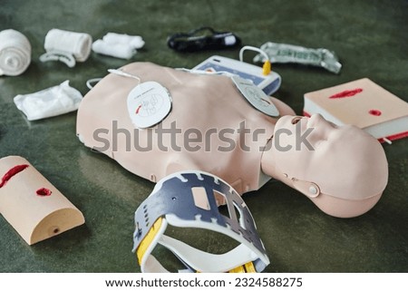 CPR training manikin near automated external defibrillator, wound care simulators, neck brace and bandages of floor in training room, medical equipment for first aid training and skills development Royalty-Free Stock Photo #2324588275