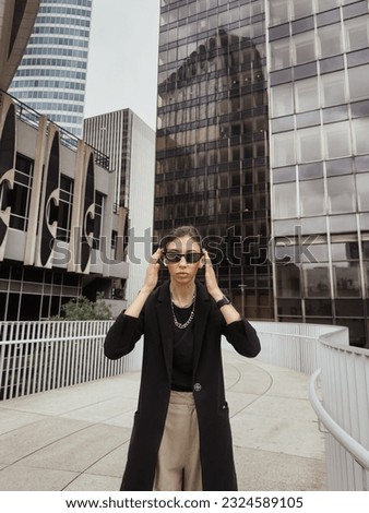 a brunette woman in office clothes and sunglasses among towers of Puteaux downtown